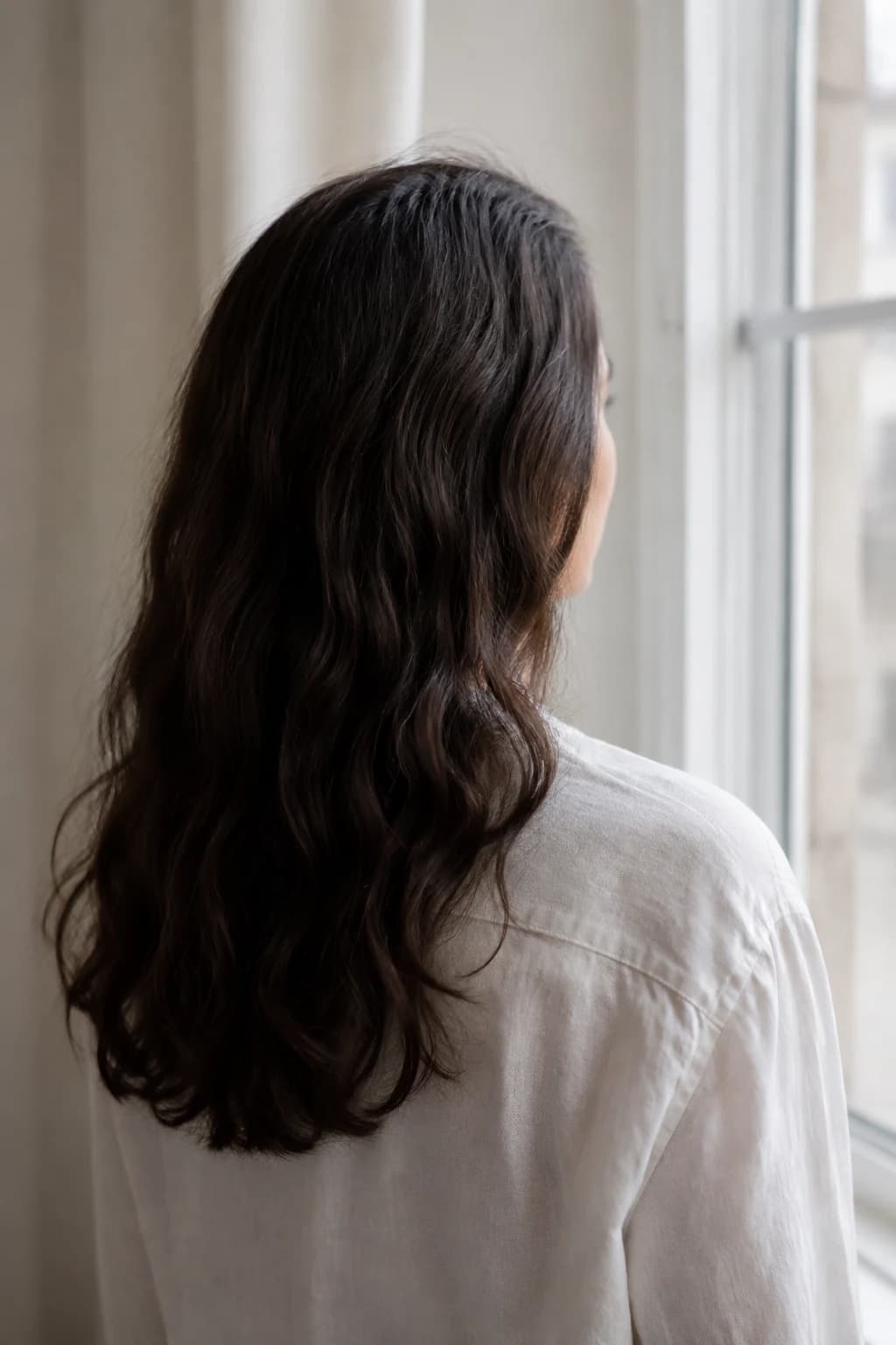 Cabello castaño con textura natural junto a una ventana. Imagen ilustrativa generada.